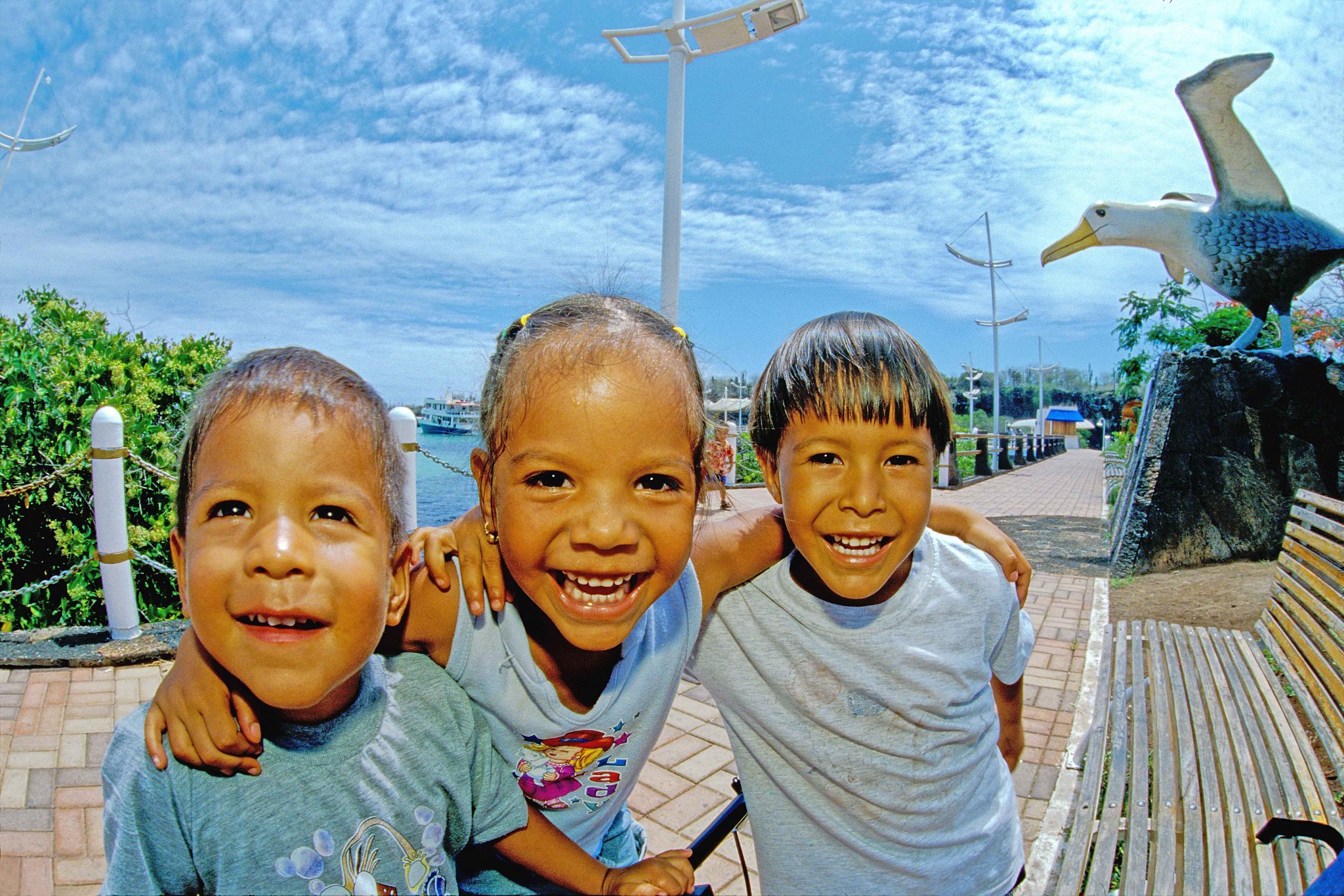 Three happy children in Puerto Ayora, near the Albatross statue in the town park.  The Galápagos Islands have the highest population growth rate in South America, which has caused  sanitation and other problems related to overpopulation within the islands.  The number of children that one sees on the streets now, compared with thirty or forty years ago, reflects this dramatic increase in population.